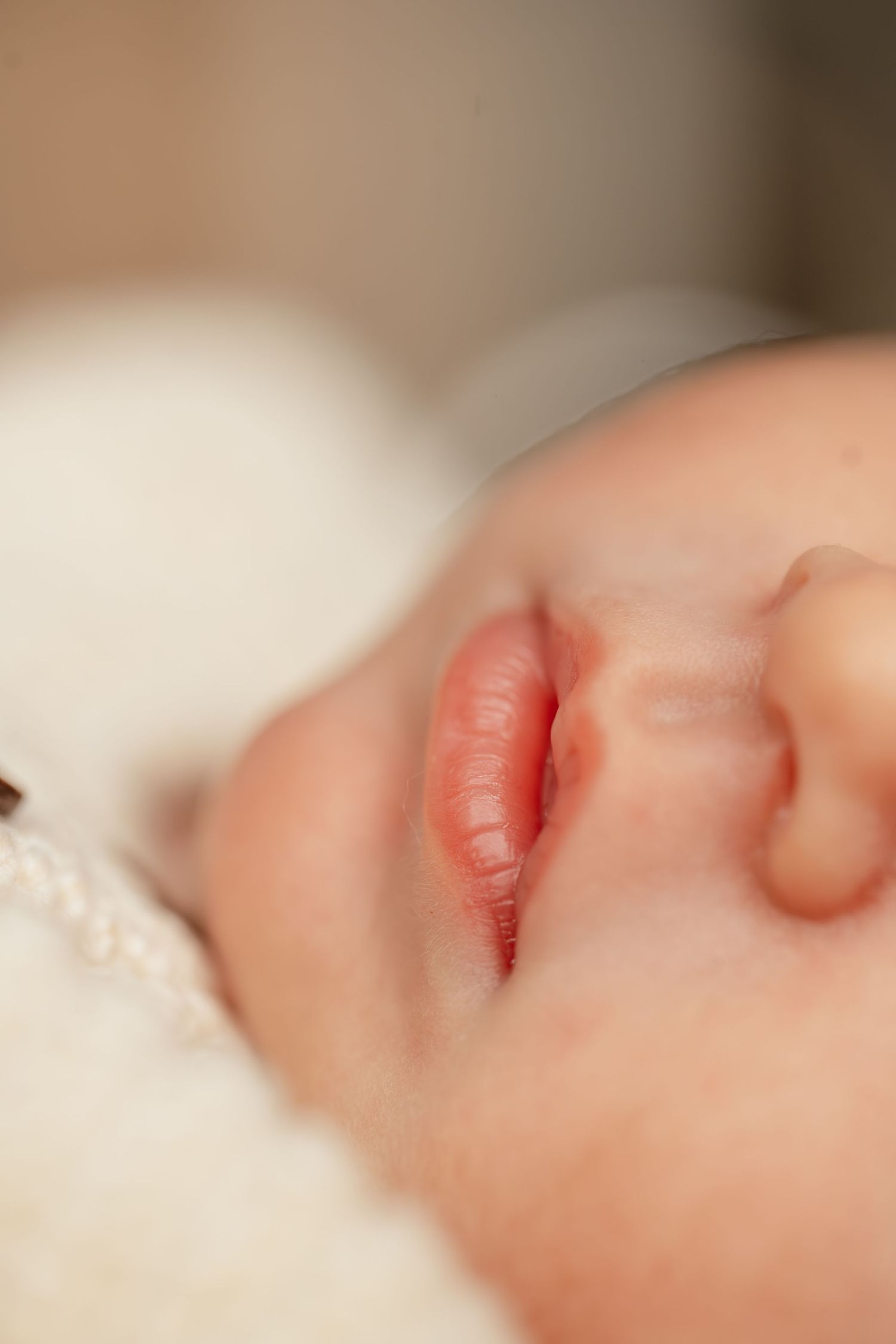 Close-up of a sleeping newborn baby's lips and nose, resting peacefully on a soft white blanket.