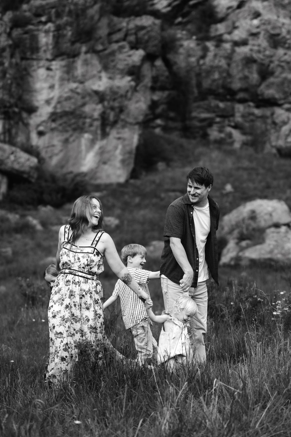 Black and white photo of a happy family with two children walking in a grassy field with rocky cliffs behind them.