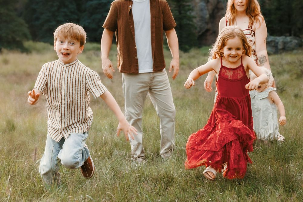Two happy children run through a green meadow during a family photo session in a scenic outdoor setting.