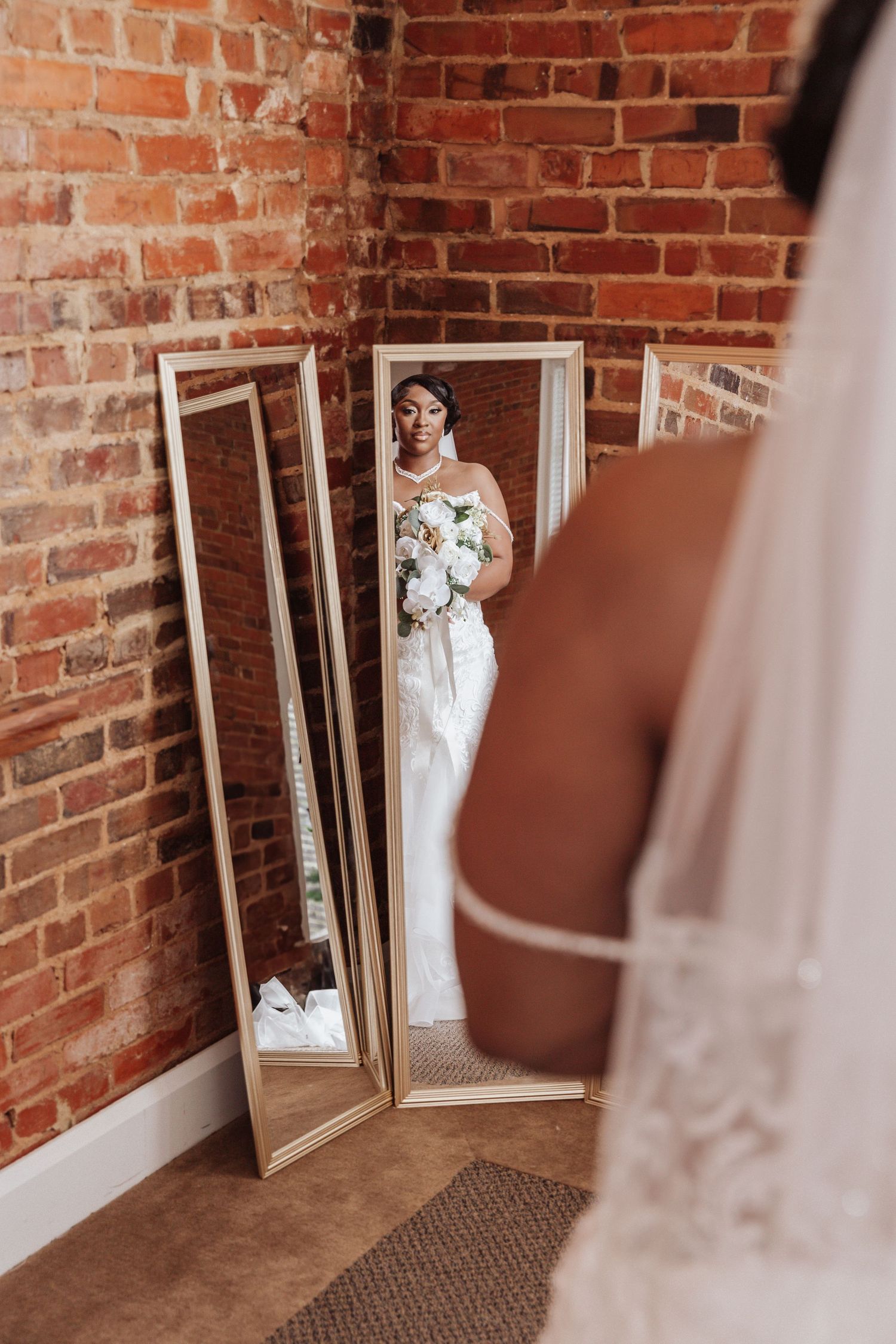 bride looking at herself on mirror wearing wedding dress and holding flower bouquet