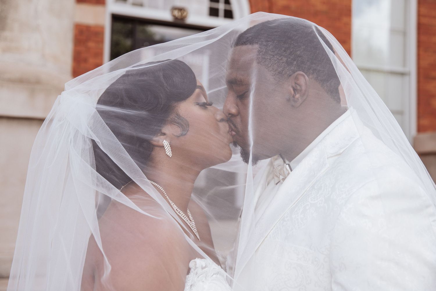 Bride and groom sharing an intimate kiss under vail with soft sunlight, romantic wedding portrait