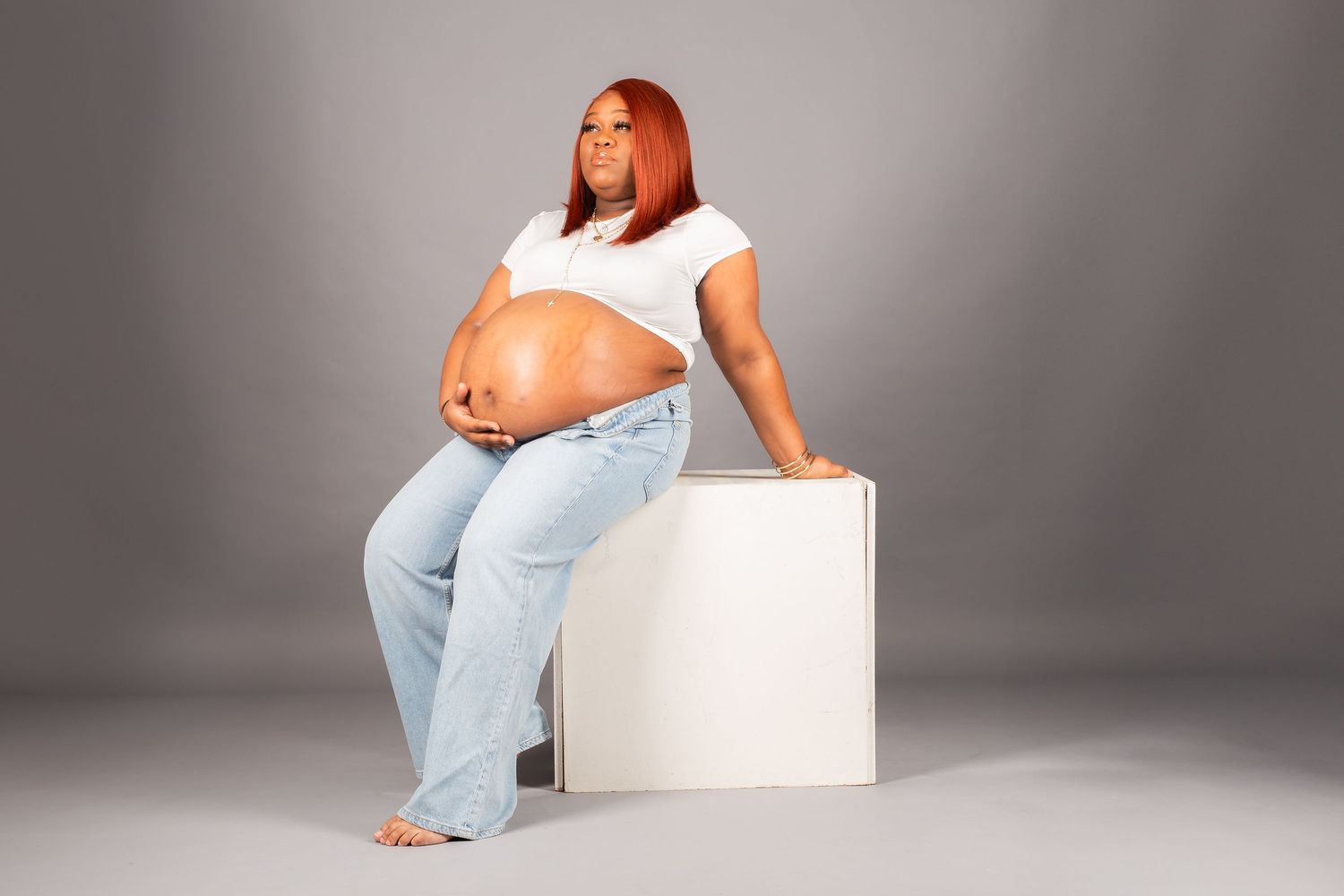 pregnant woman wearing jeans and white shirt with gray backdrop in studio