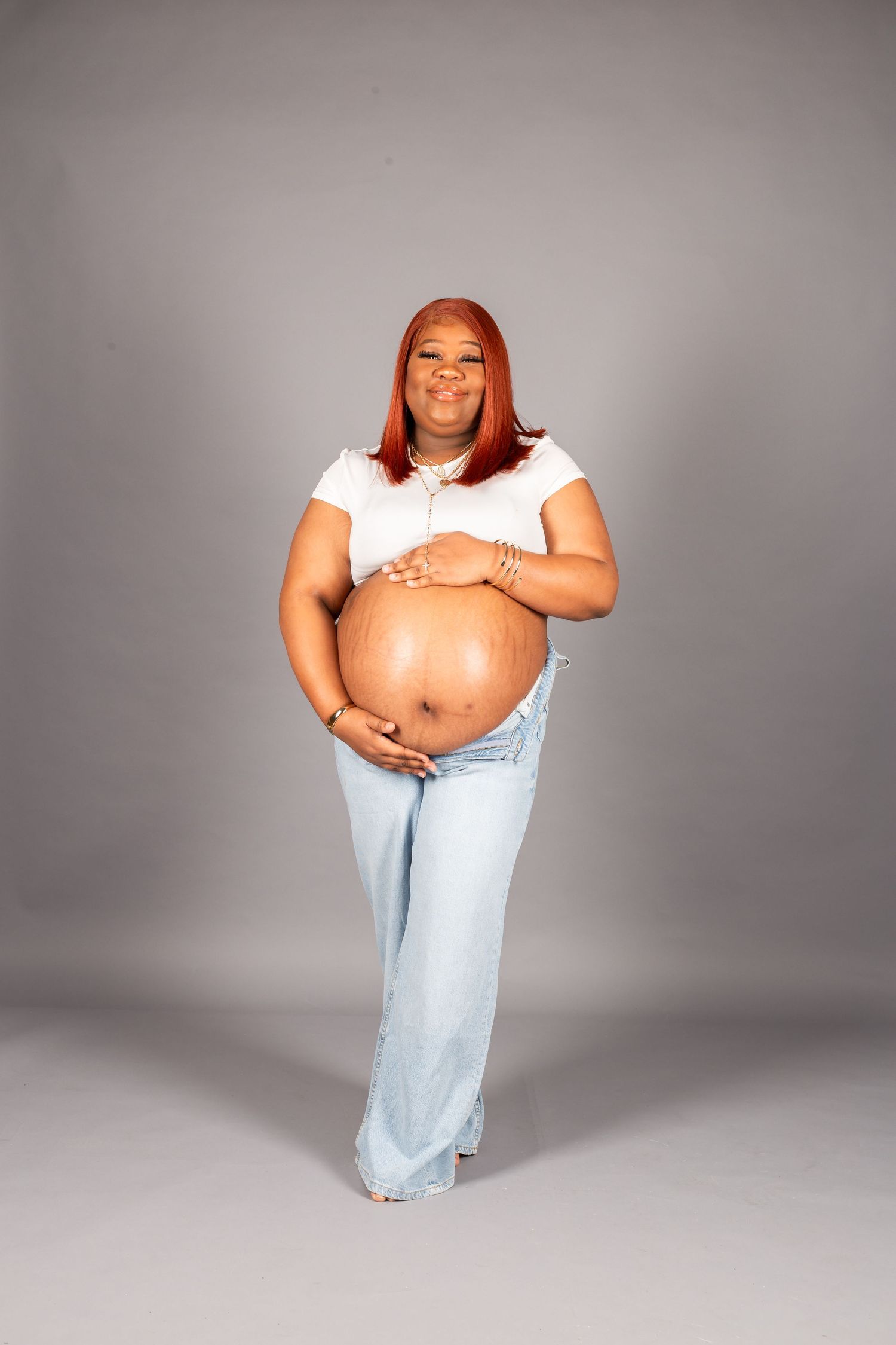 pregnant woman wearing jeans and white shirt with gray backdrop in studio