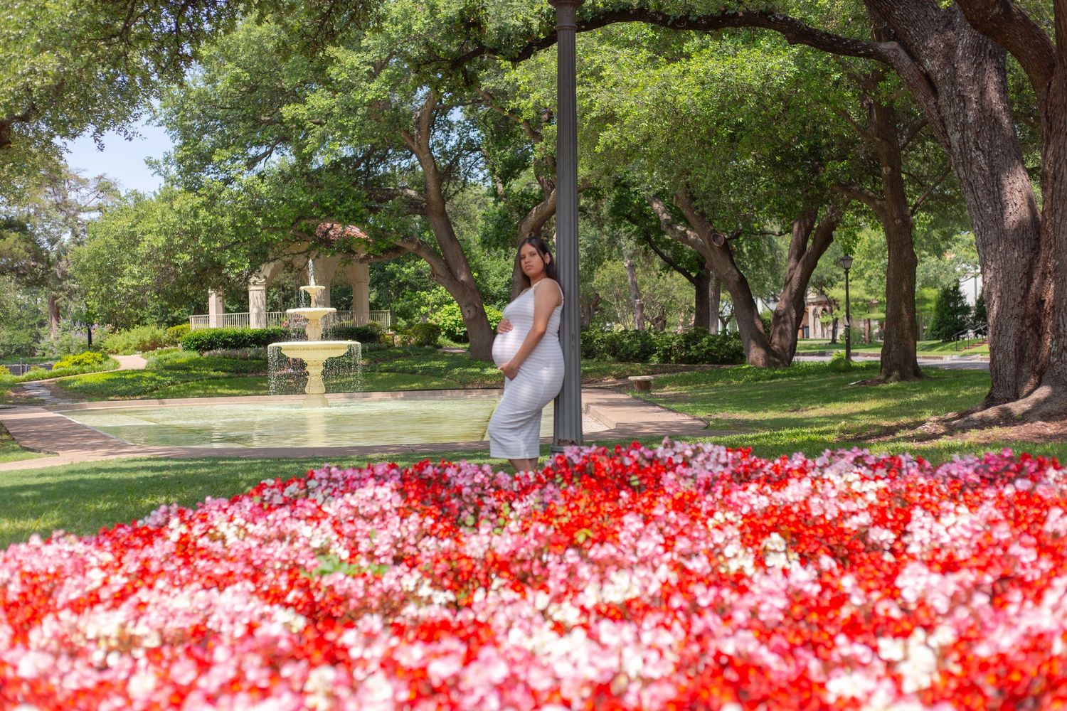 pregnant woman leaning on post in garden by water fountain