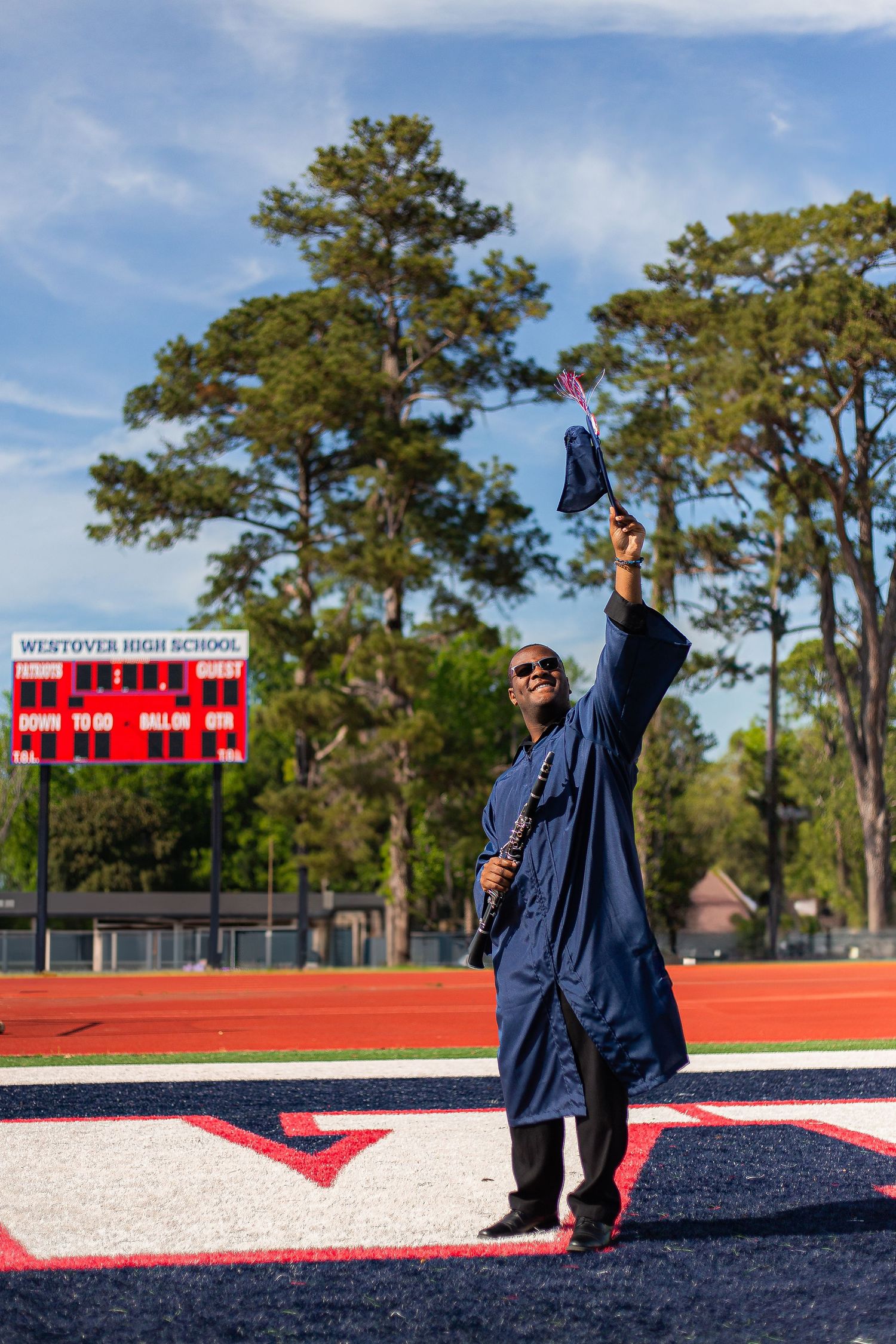 high school graduate holding instrument and throwing cap in football field