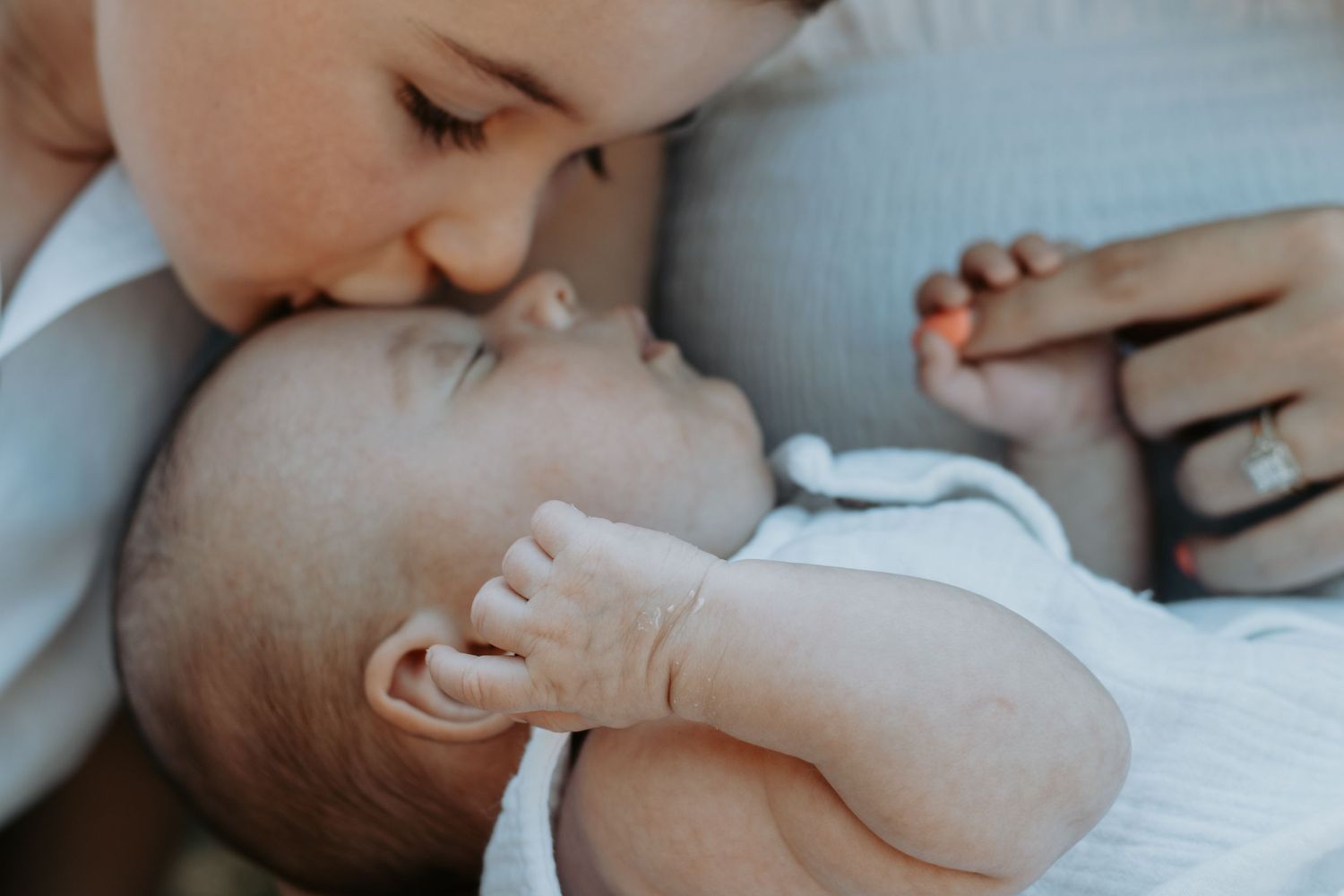Close-up of tiny newborn baby feet cradled gently in mother's hands, wearing a white onesie.
