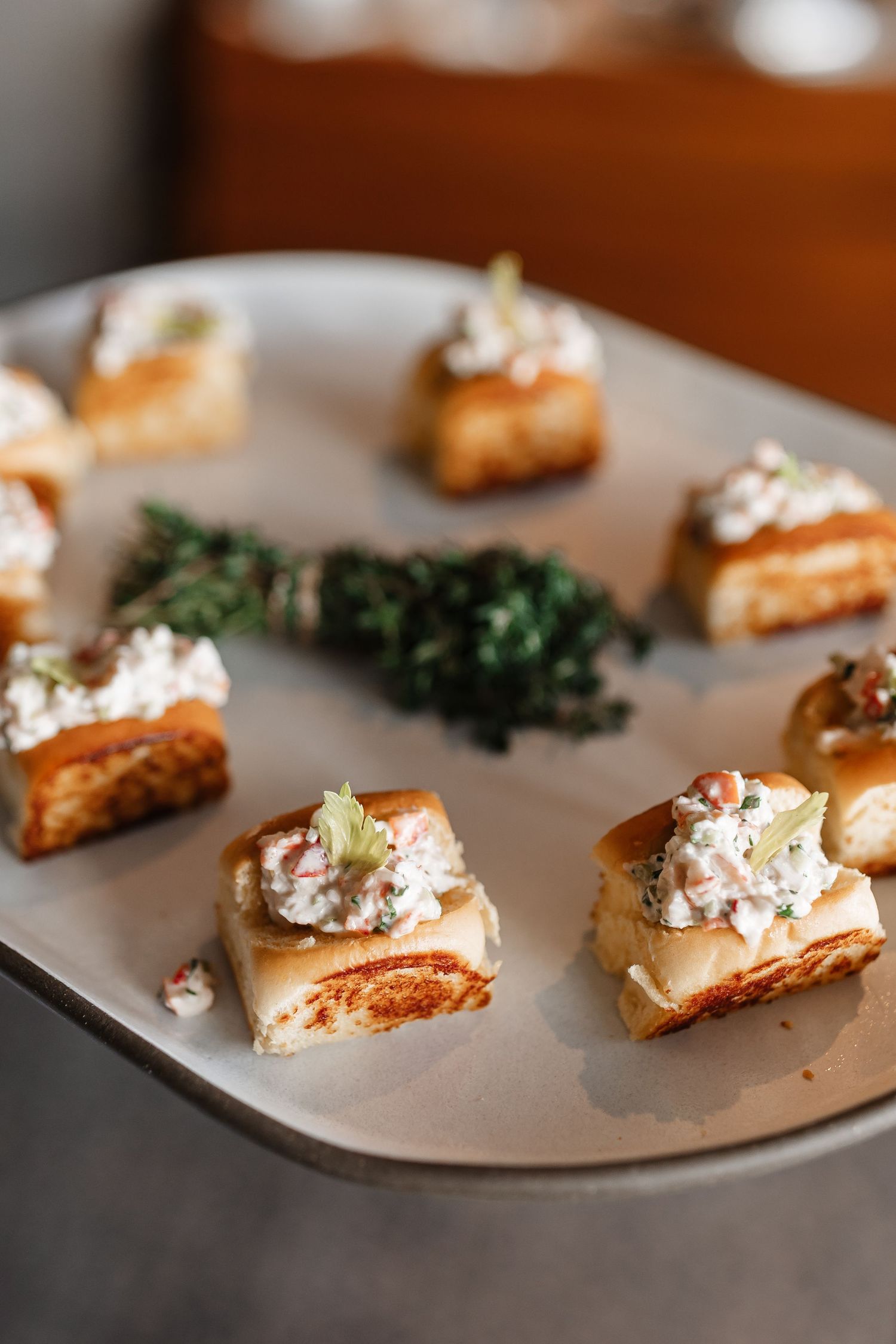 Elegant appetizer canapes with creamy herb topping on toasted bread squares, served on a silver platter.