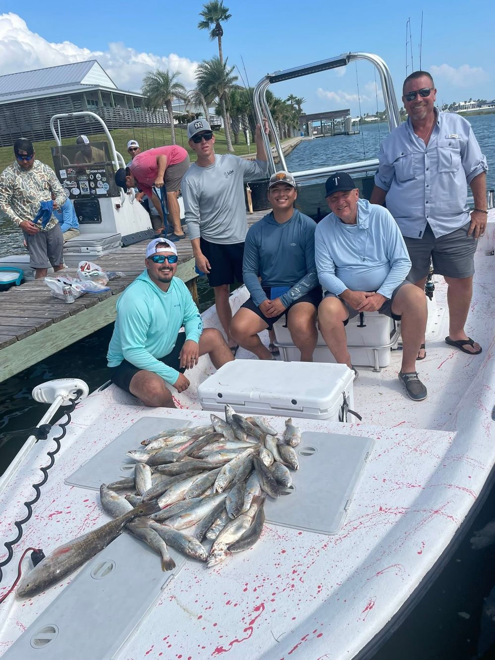 Happy fishing group posing with large speckled trout catch on boat at marina dock.