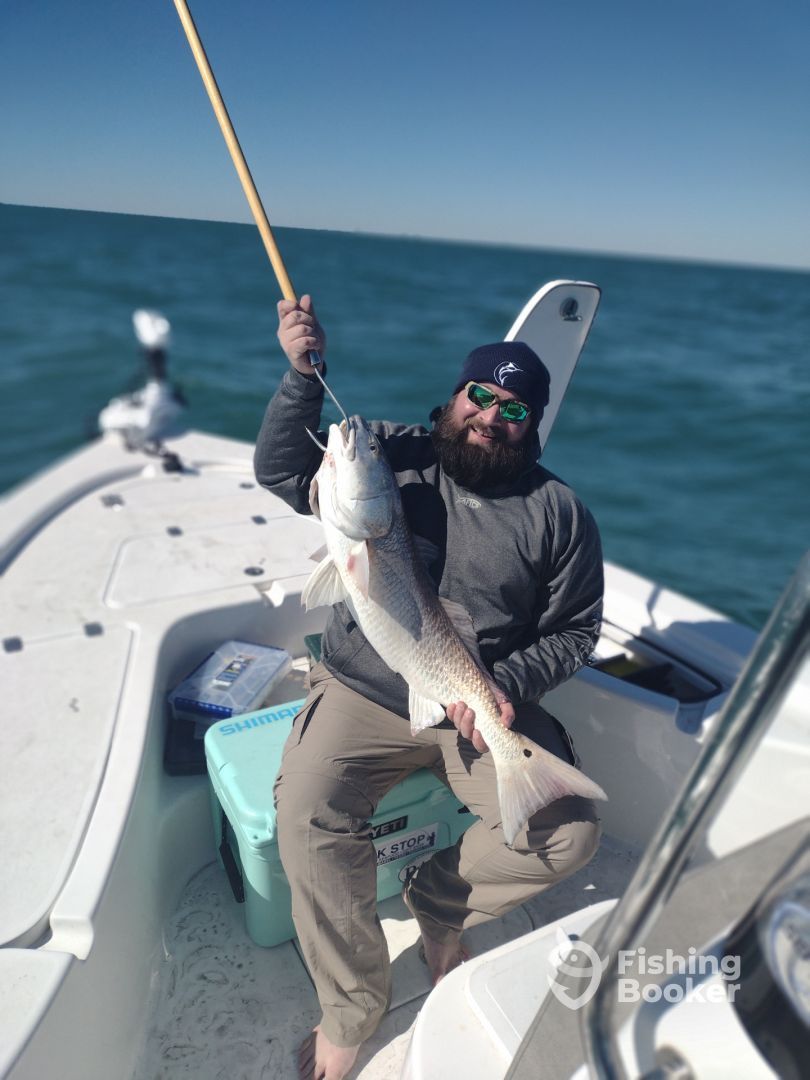 Angler holding large redfish caught on a fishing charter in clear blue Gulf waters.