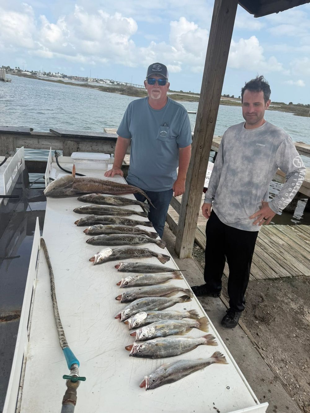 Two men standing beside a large catch of redfish and trout laid out on a dock cleaning table.