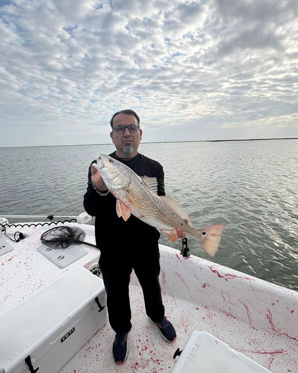Angler displaying a large redfish on a fishing boat with cloudy Texas coastal skies.