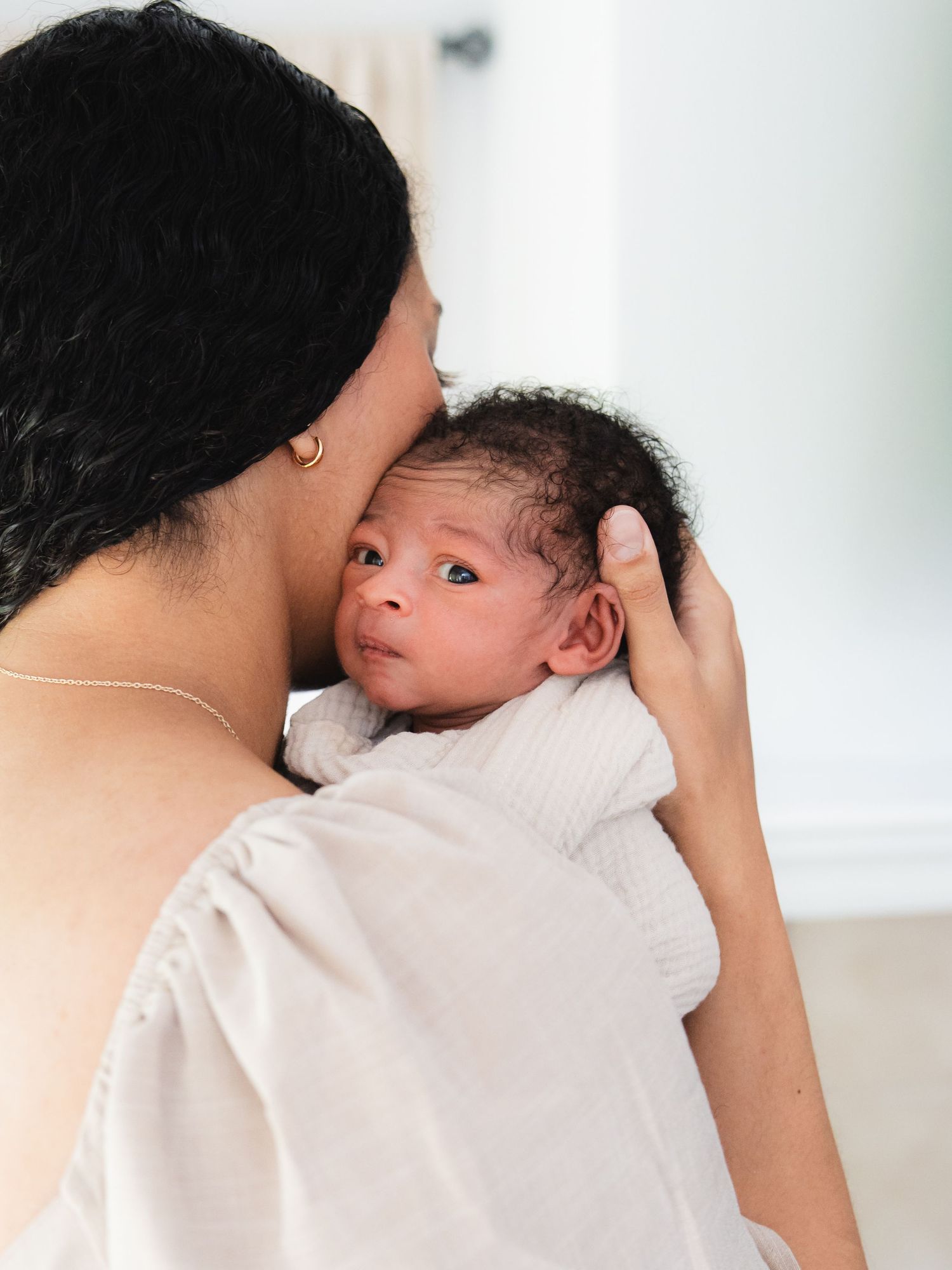 A mother tenderly kisses her newborn baby's head while cradling the infant against her shoulder.
