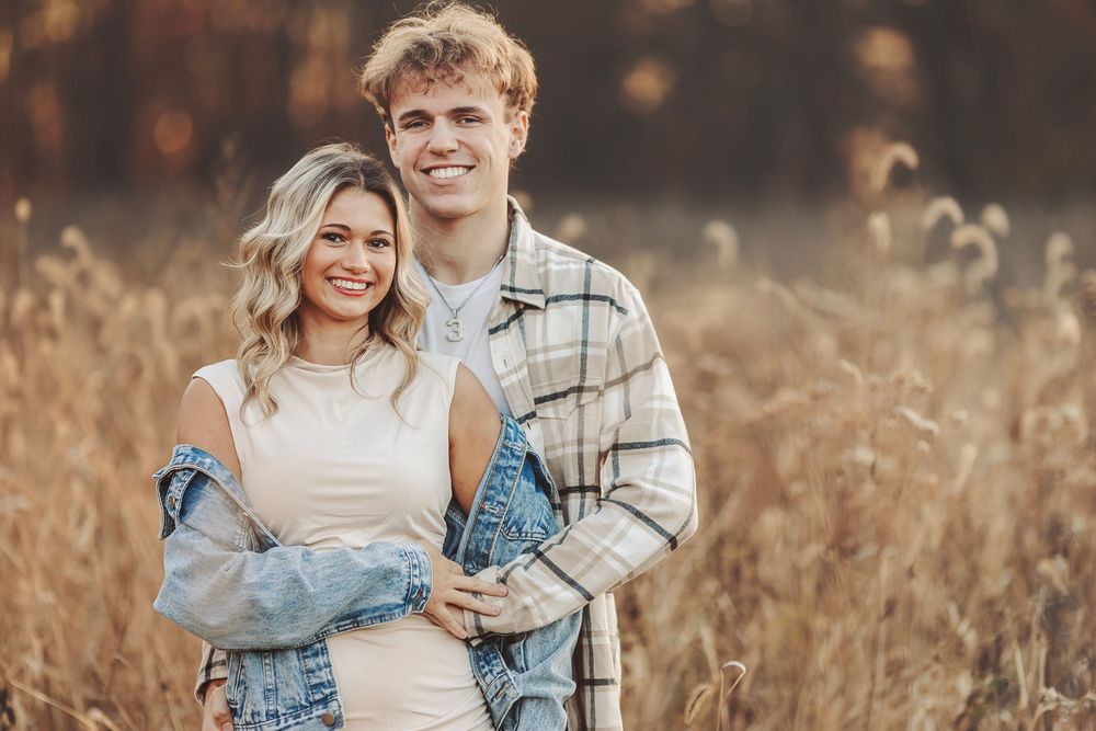 Couple embracing outdoors in golden autumn light, smiling warmly among fall foliage for an engagement photo.