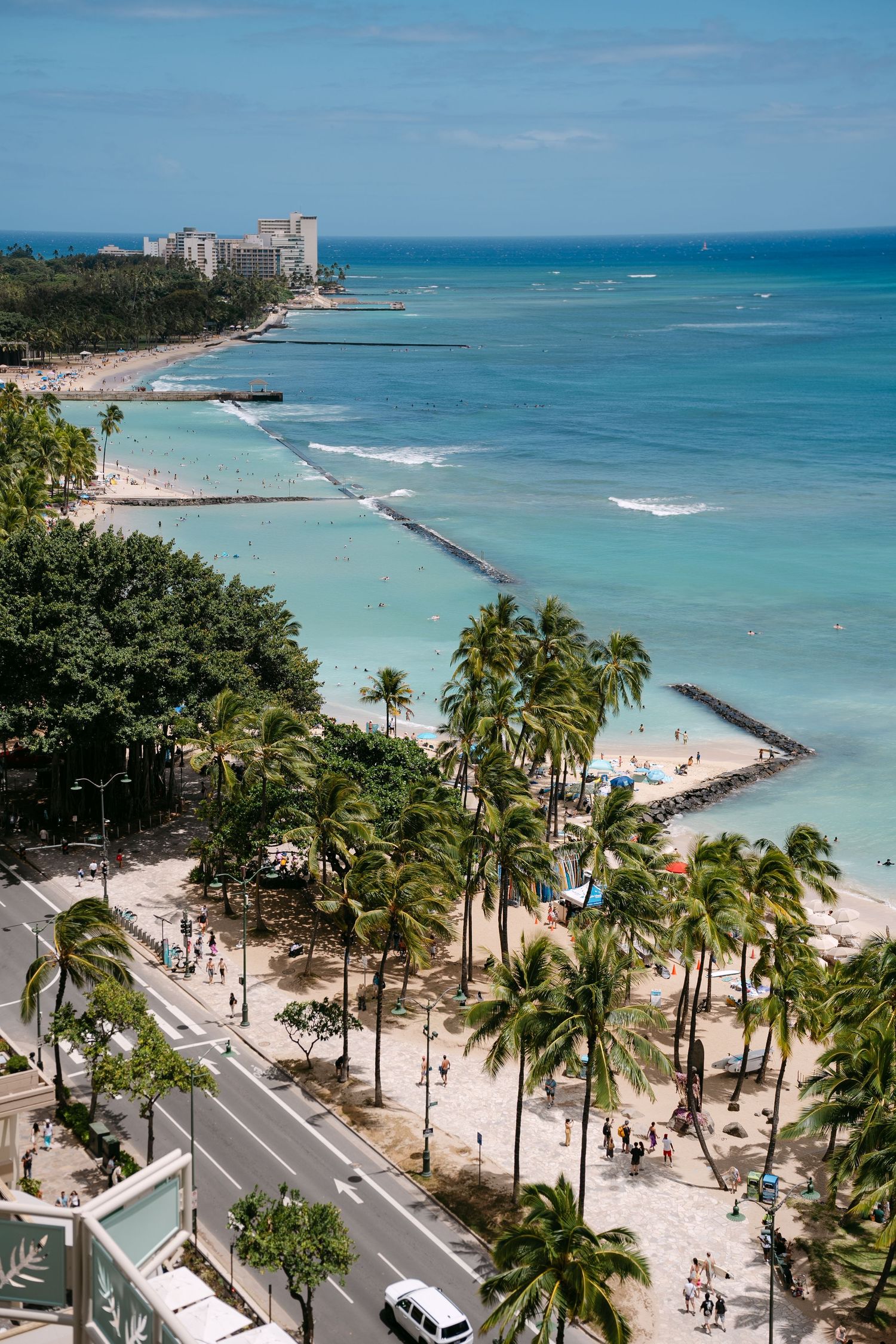 Aerial view of Waikiki Beach in Hawaii with turquoise waters, palm trees, sandy shores, and city hotels in the distance.