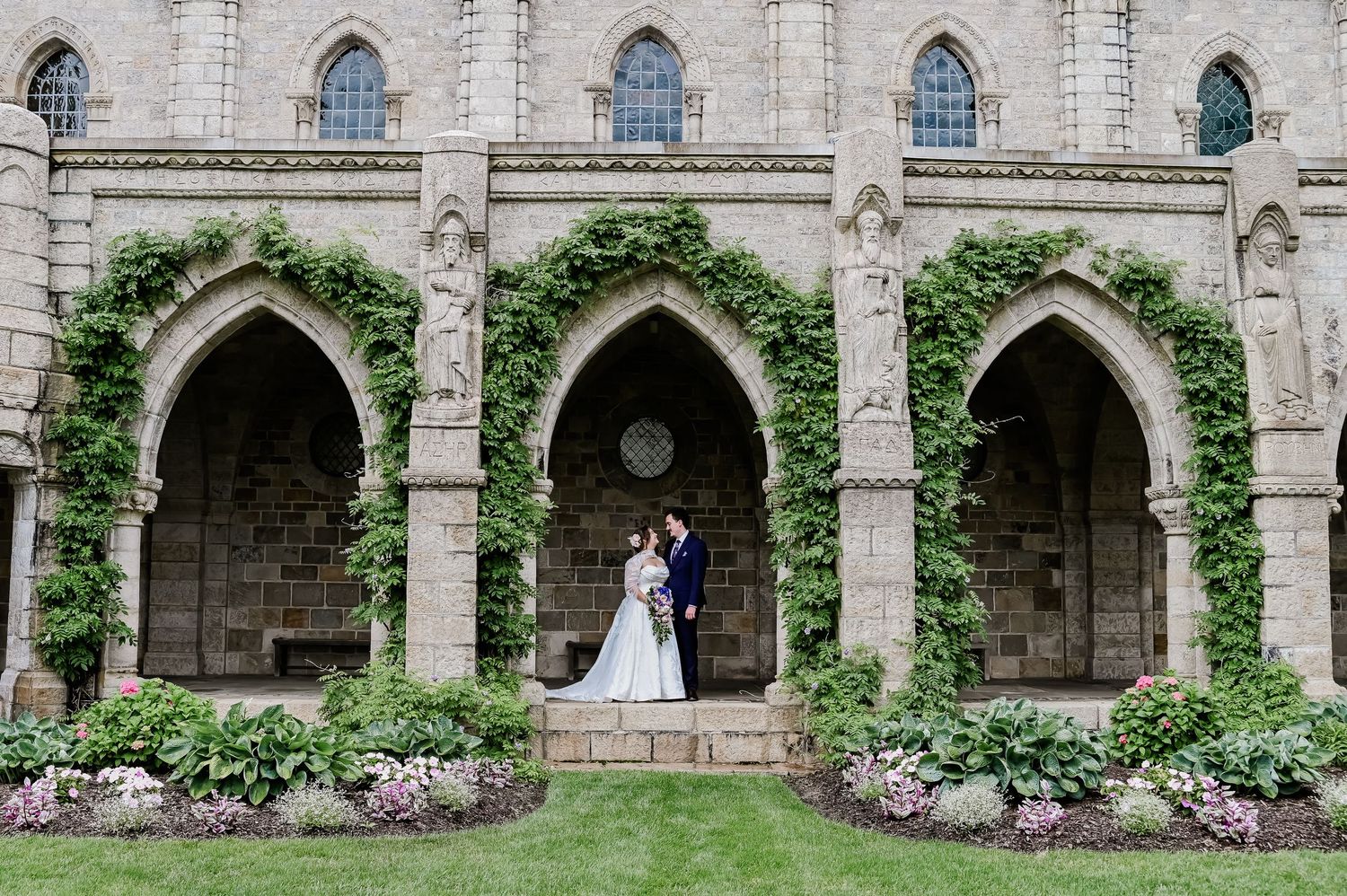 Bride and groom sitting together on stone steps overlooking lush green garden landscape at outdoor wedding venue.
