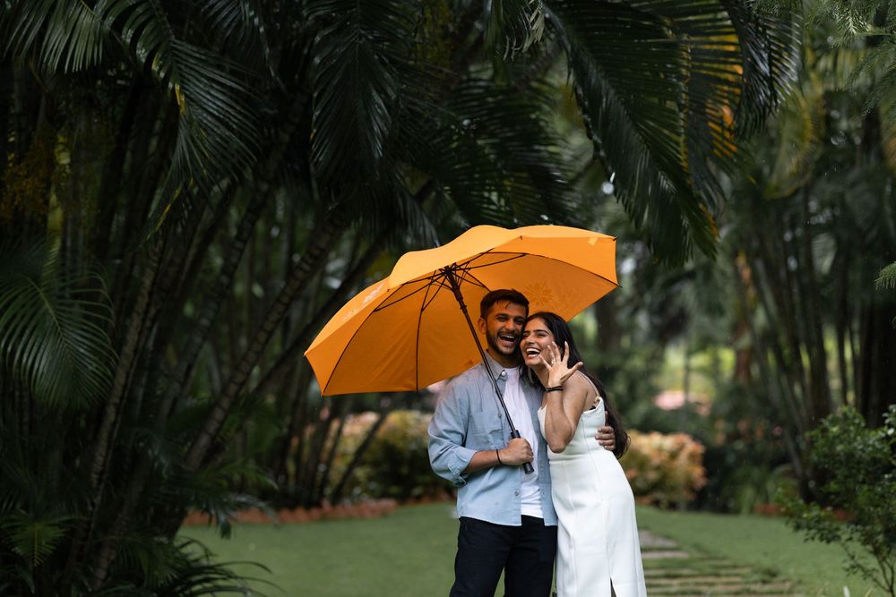 Romantic couple embracing under an orange umbrella in a lush tropical garden pathway.