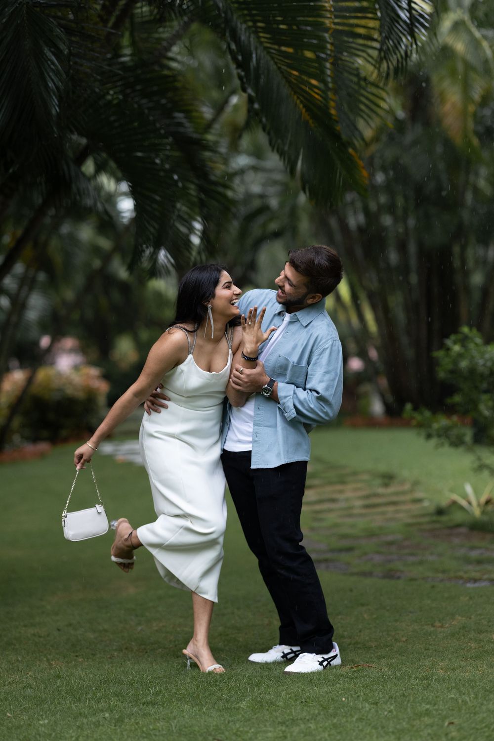 Happy couple laughing and dancing together on green grass surrounded by tropical palm trees.
