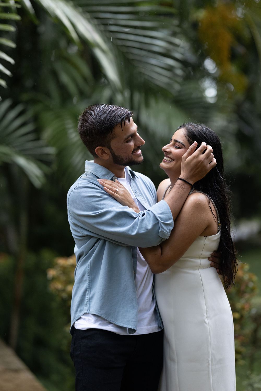 Romantic couple embracing tenderly in a tropical garden, man gently holding woman's face while smiling.