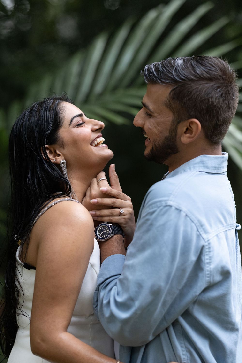 Couple sharing a joyful intimate moment, man tenderly holding woman's face as she laughs in tropical setting.