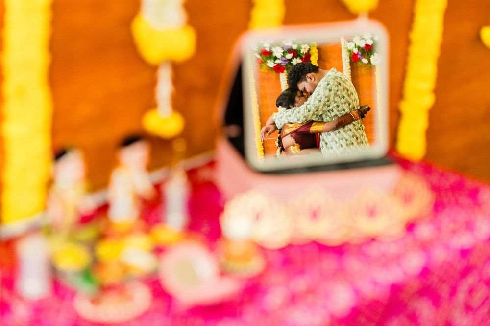 Indian wedding ceremony reflected in a mirror, surrounded by colorful floral decorations and pink petals.