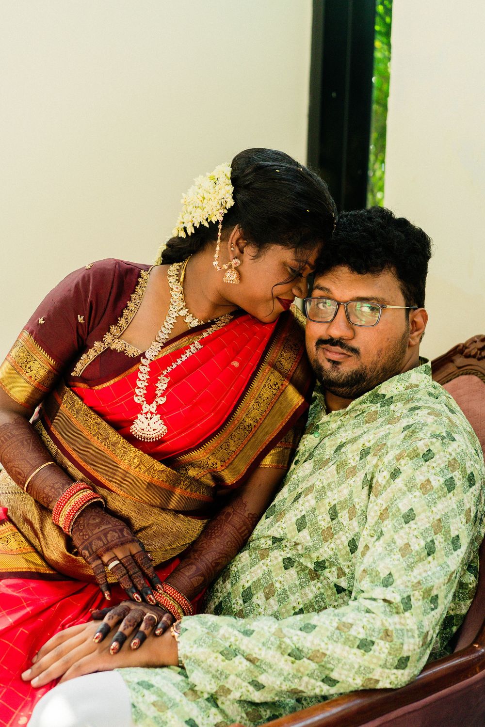 Indian bride in red silk saree with gold jewelry leans on groom in green kurta during traditional wedding ceremony.