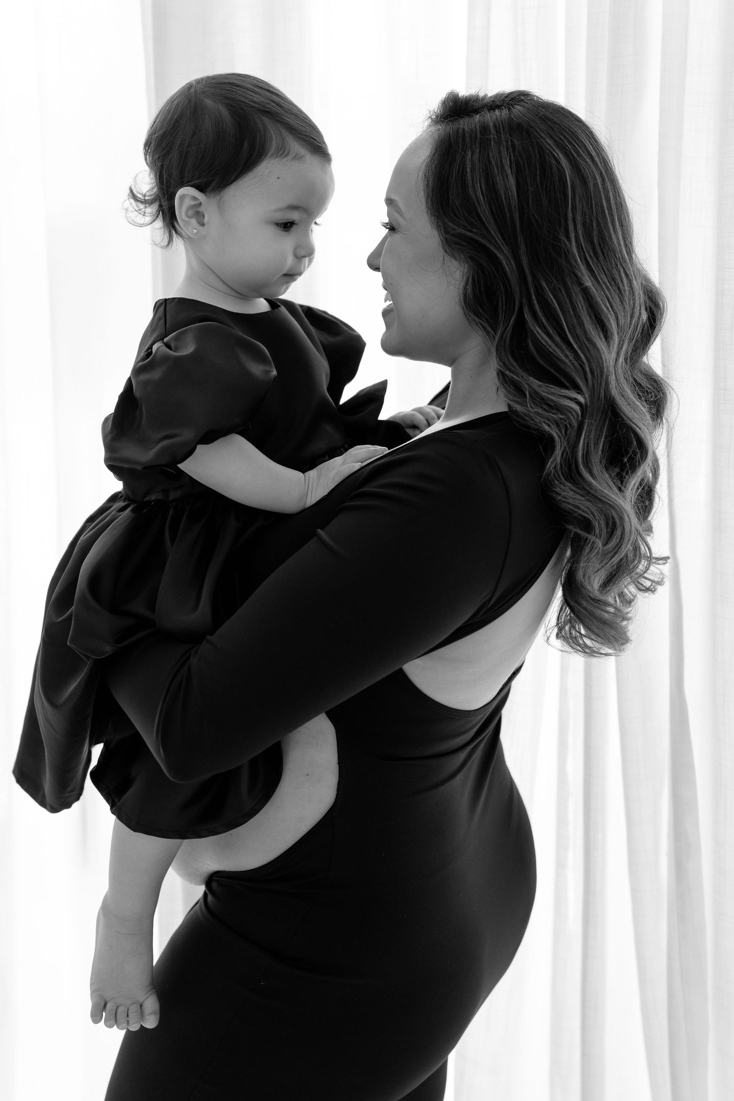 Black and white photo of a pregnant woman in a black dress holding a toddler girl in a matching black dress.