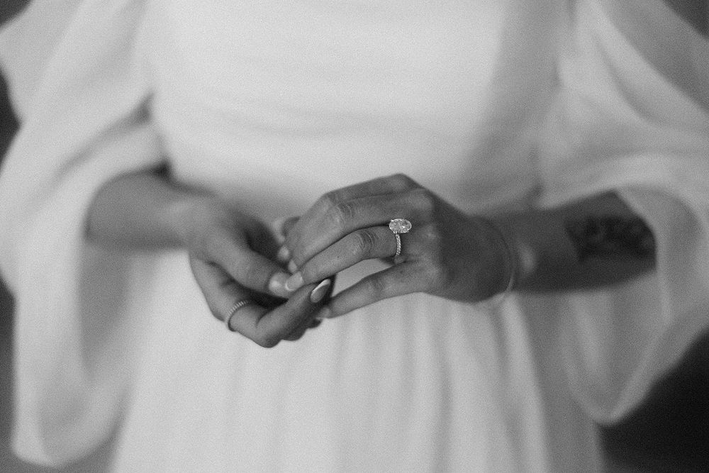 Black and white photo of a bride in white dress showcasing her diamond engagement ring and tattoo on her wrist.