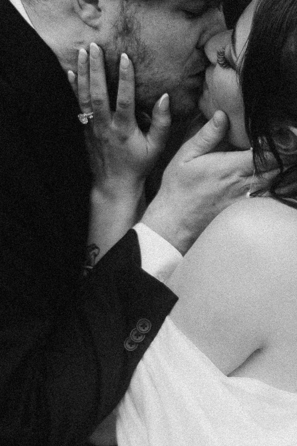 Close-up black and white photo of bride and groom sharing intimate wedding kiss with diamond ring visible.