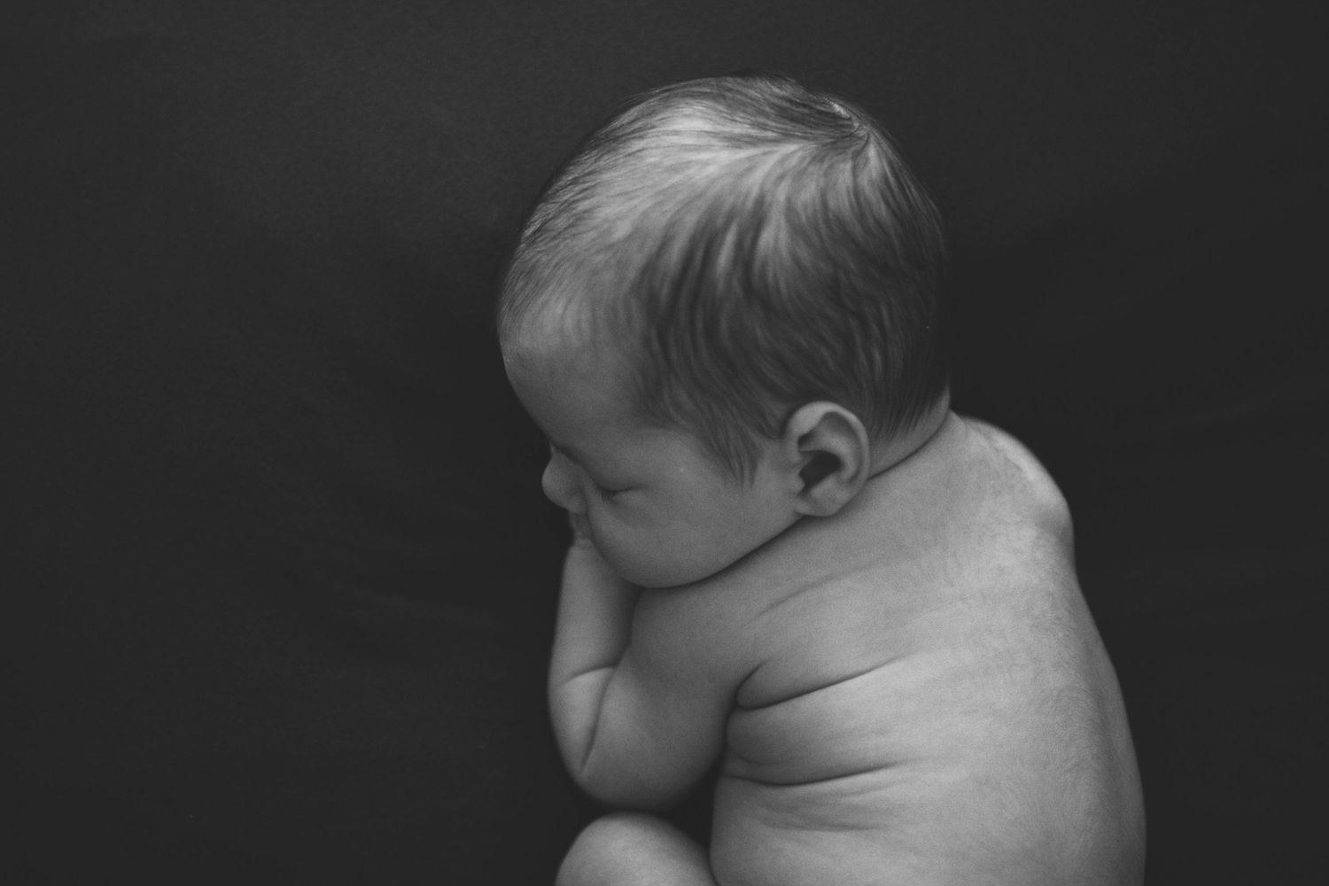 Peaceful newborn baby sleeping in a wooden bowl, wearing a green knit bonnet, wrapped in a soft green blanket.