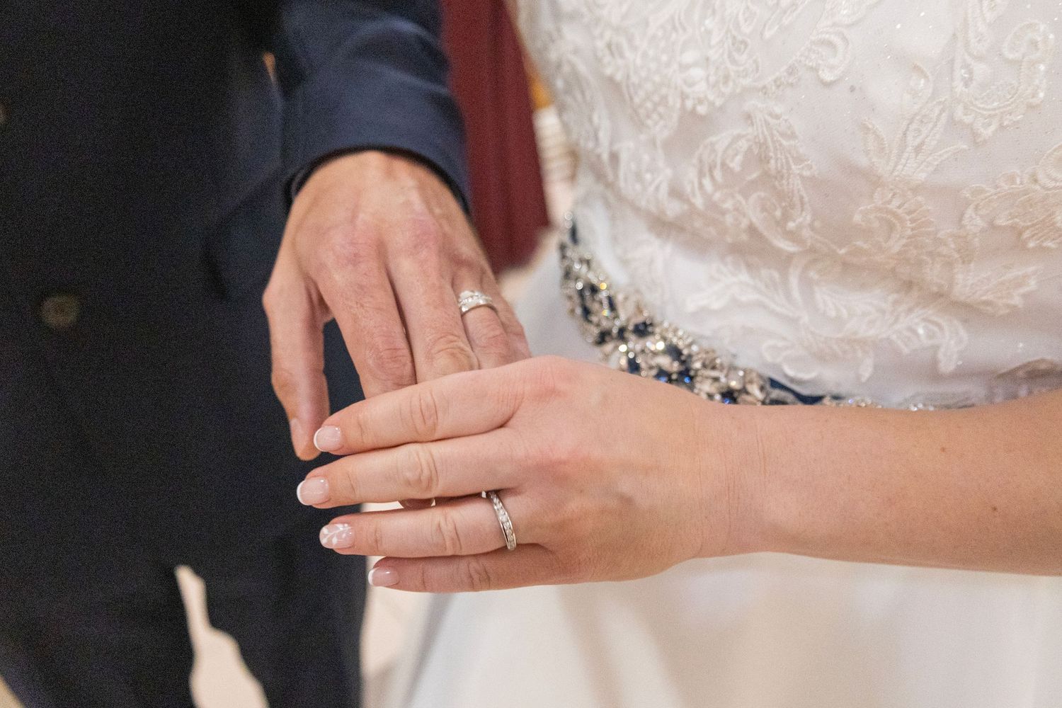 Close-up of bride and groom exchanging wedding rings during ceremony, showcasing elegant bridal gown and diamond rings.