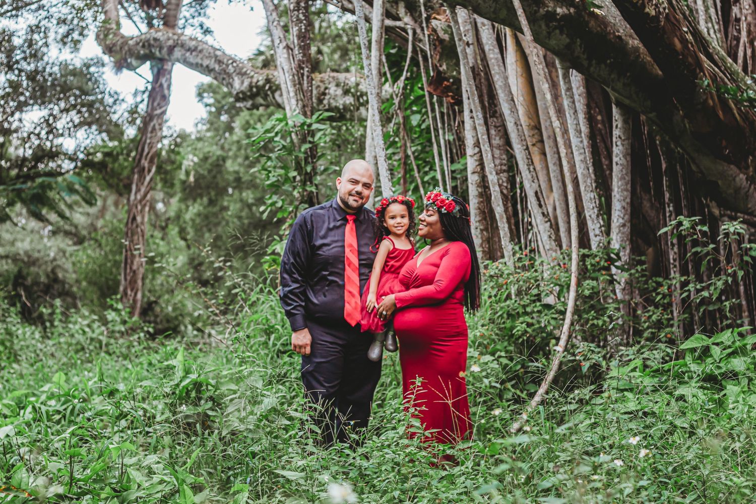 Couple in red maternity photoshoot surrounded by lush greenery and bamboo trees outdoors at riverbend park Jupiter.