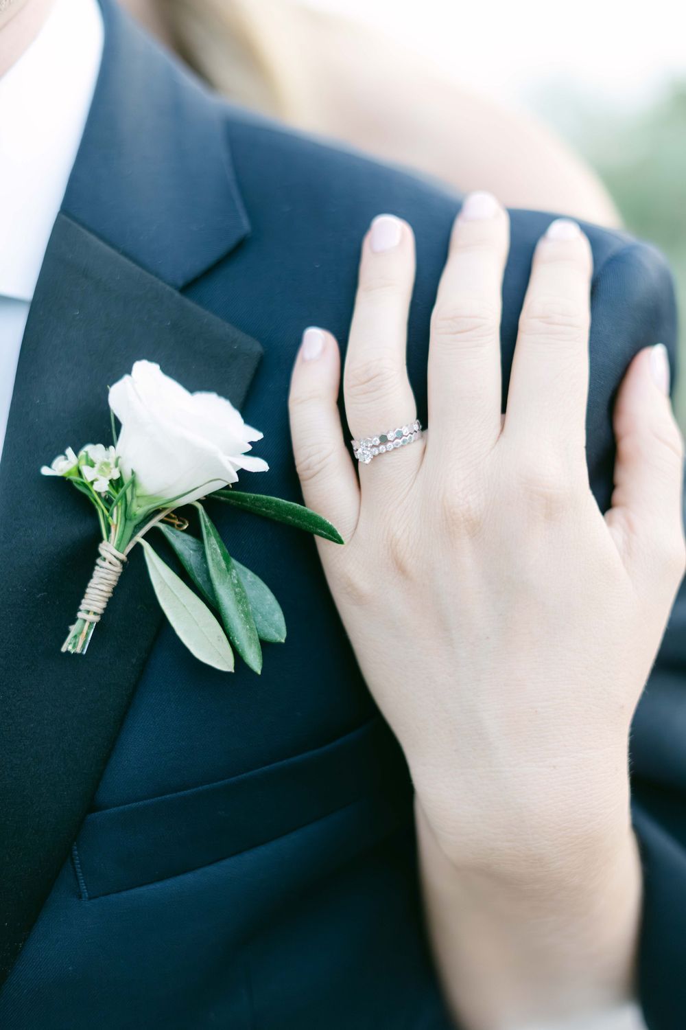 Close-up of bride's diamond wedding rings on groom's lapel beside white rose boutonniere.