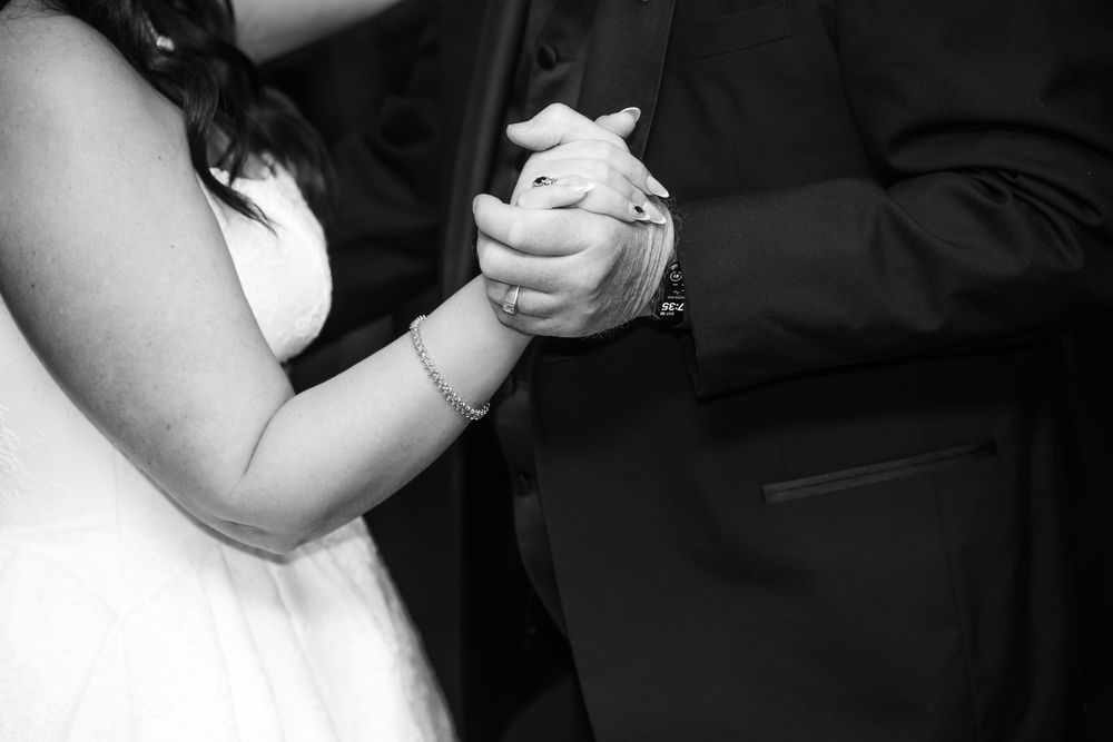 Black and white close-up of a bride in a white dress holding hands with a man in a dark suit during a wedding dance.