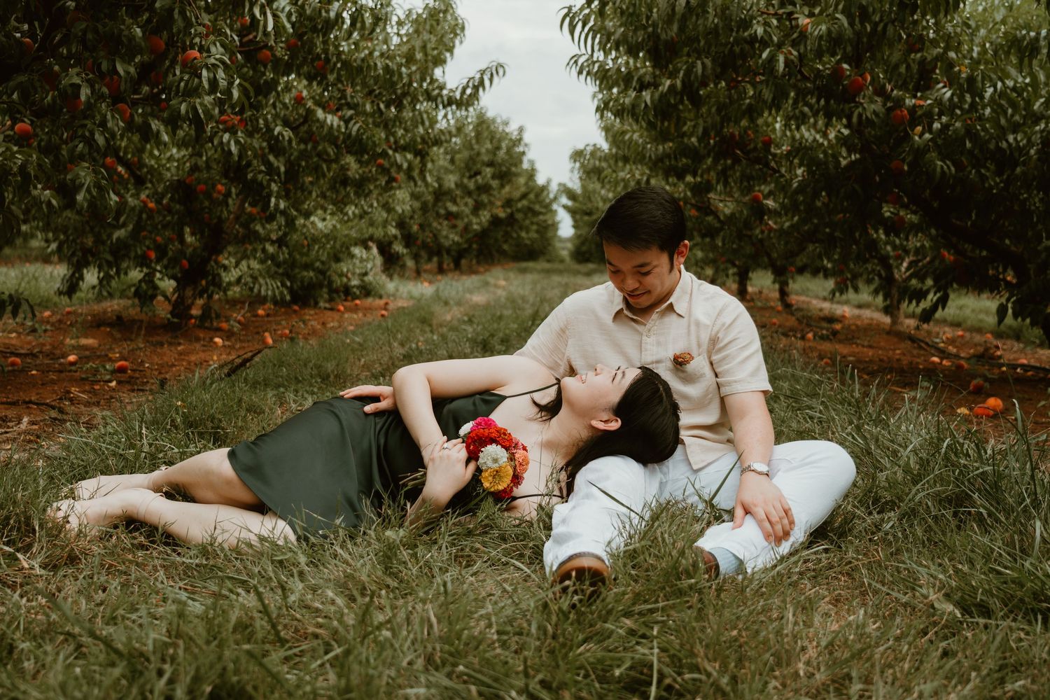 Couple relaxing in a lush orchard, woman lying in mans lap surrounded by fruit trees in a romantic outdoor setting.