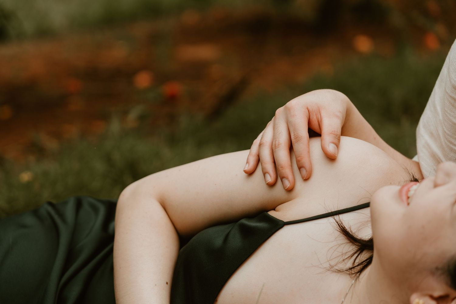 Woman lying on grass in a dark green dress, resting her hand on her knee in a serene outdoor setting.