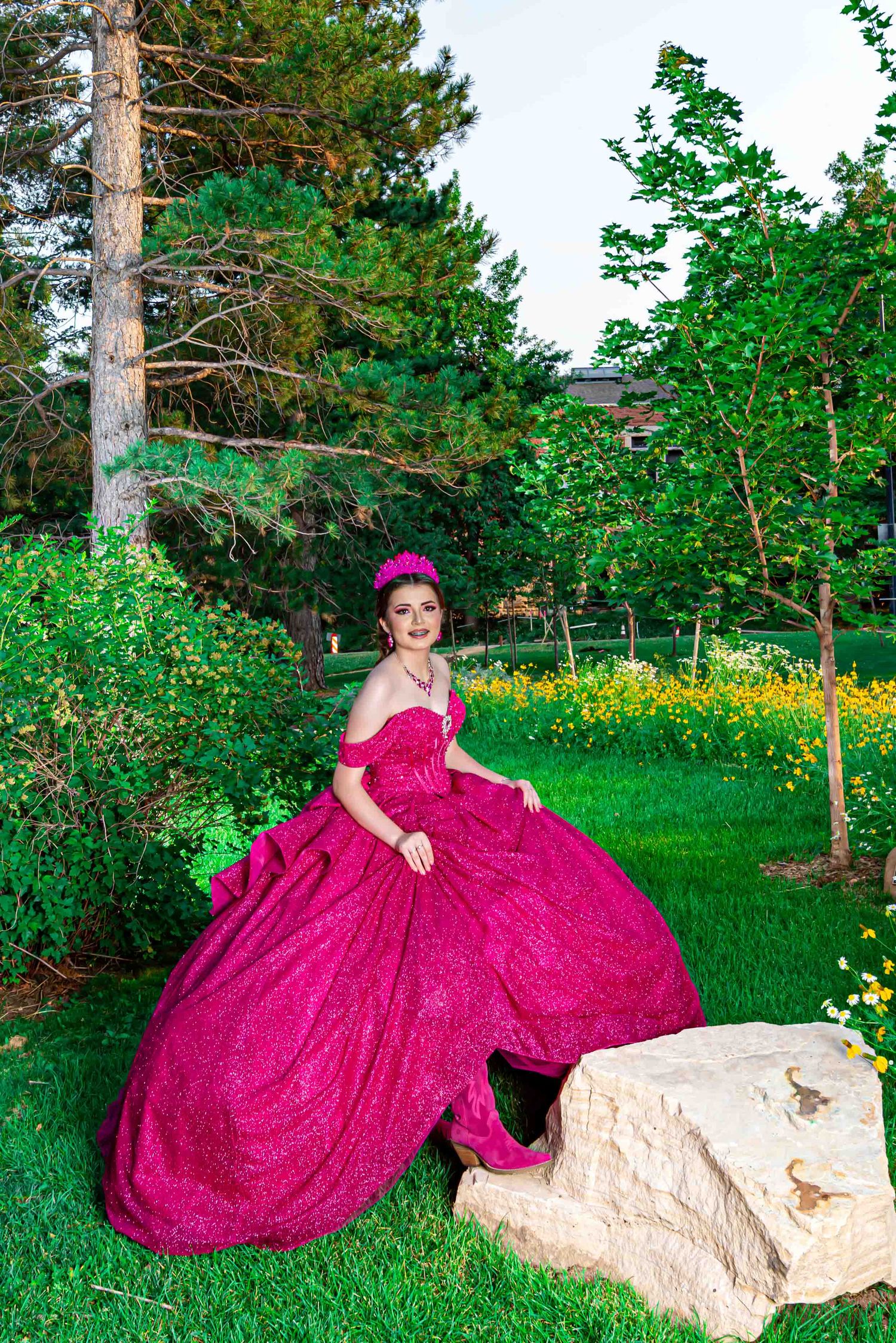 A young woman in a vibrant magenta ball gown poses gracefully in a lush green garden setting.