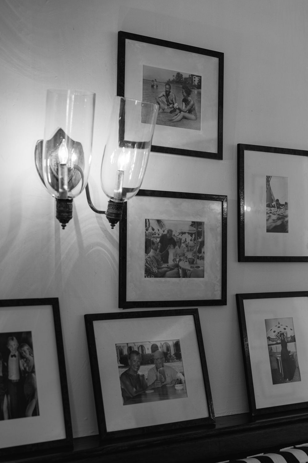 Black and white photo wall display with framed vintage photographs and elegant glass wall sconces on a light wall.