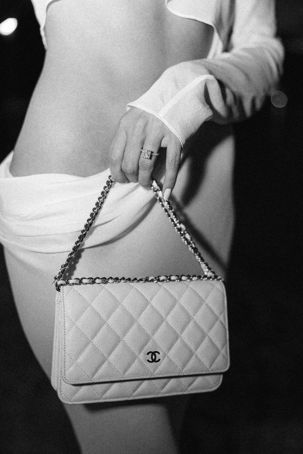 Black and white photo of a woman holding a quilted Chanel WOC bag with chain strap and CC logo.