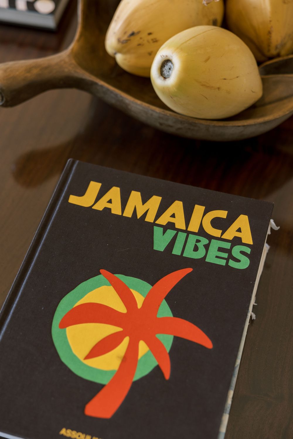 Jamaica Vibes book by Assouline on a wooden table with a bowl of tropical fruit in the background.
