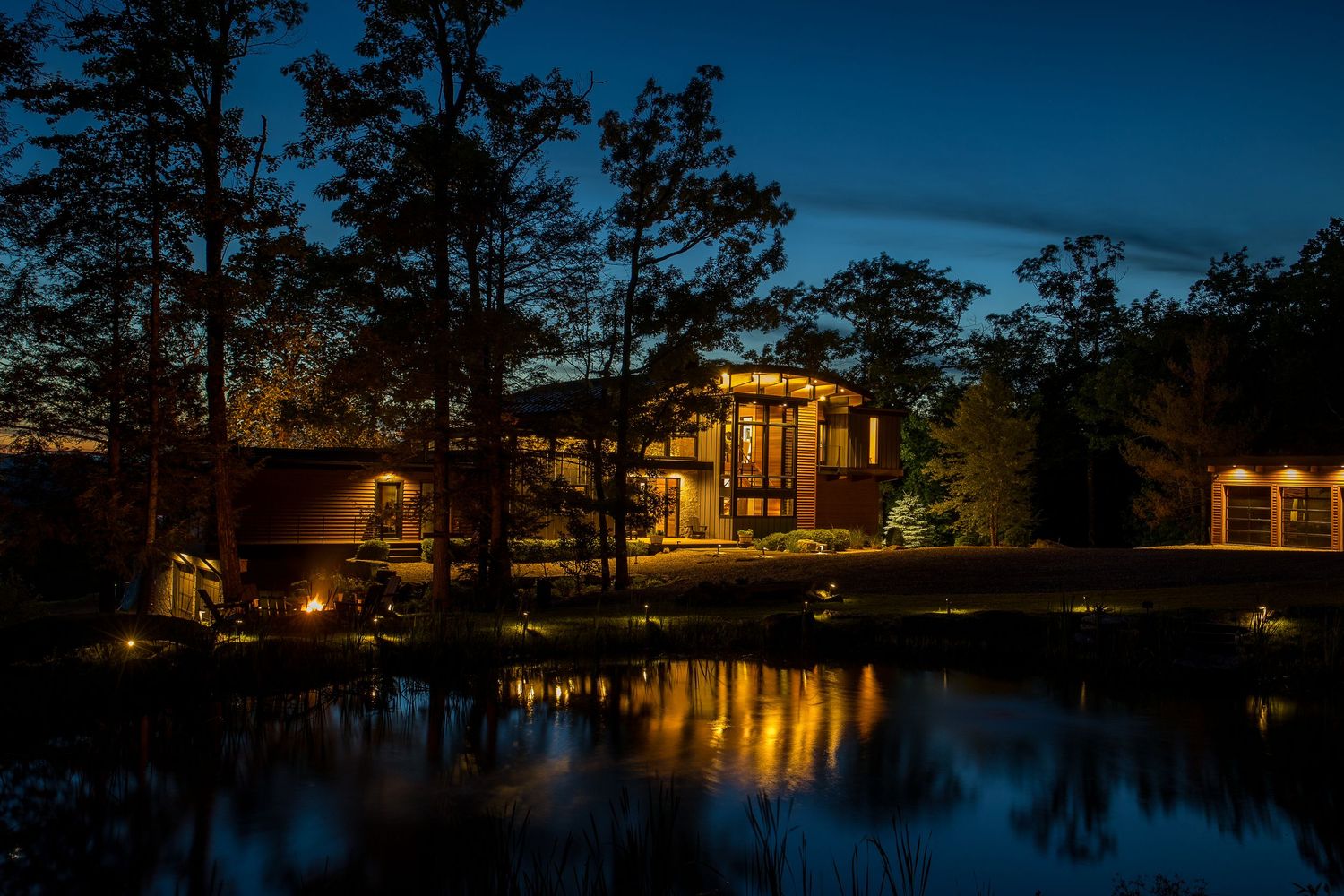 Stunning lakeside home illuminated at night with warm lights reflecting beautifully on the calm water surface.