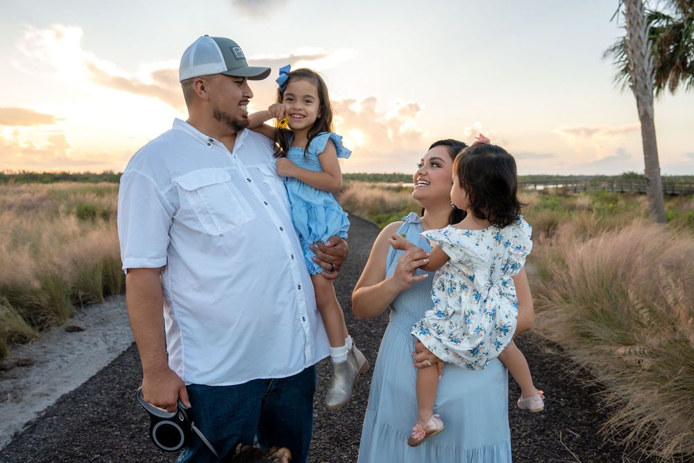 Family of four enjoying a sunset outdoor photo session, parents holding young daughters on a scenic path.