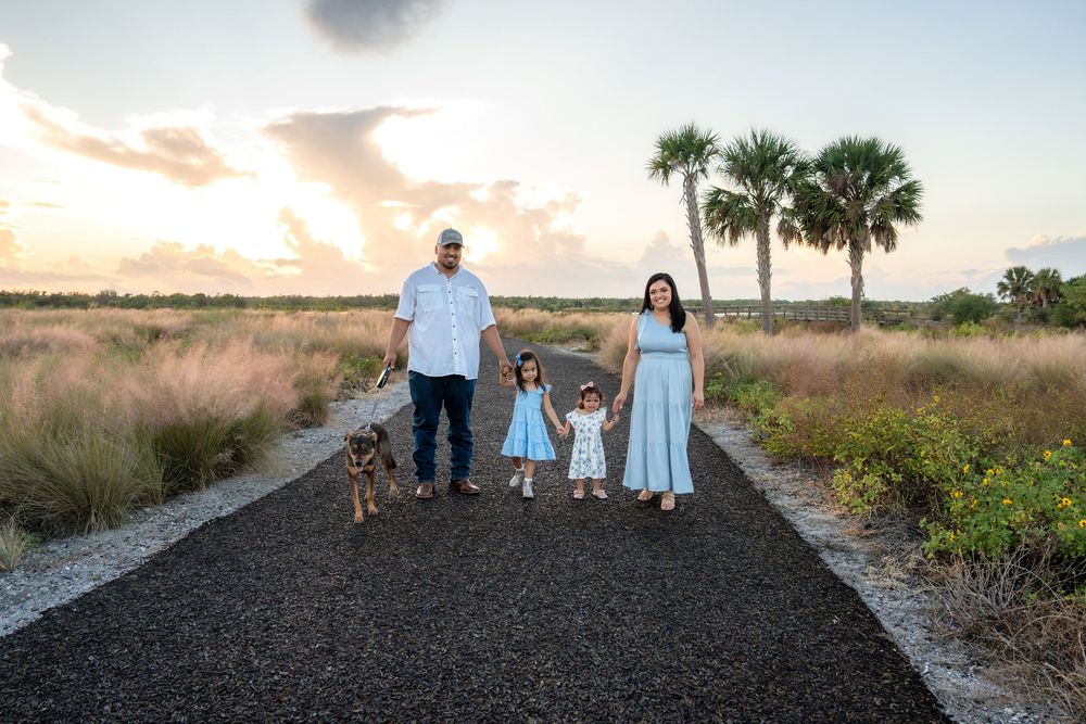 Family of four with dog posing on path at sunset near palm trees in Florida.