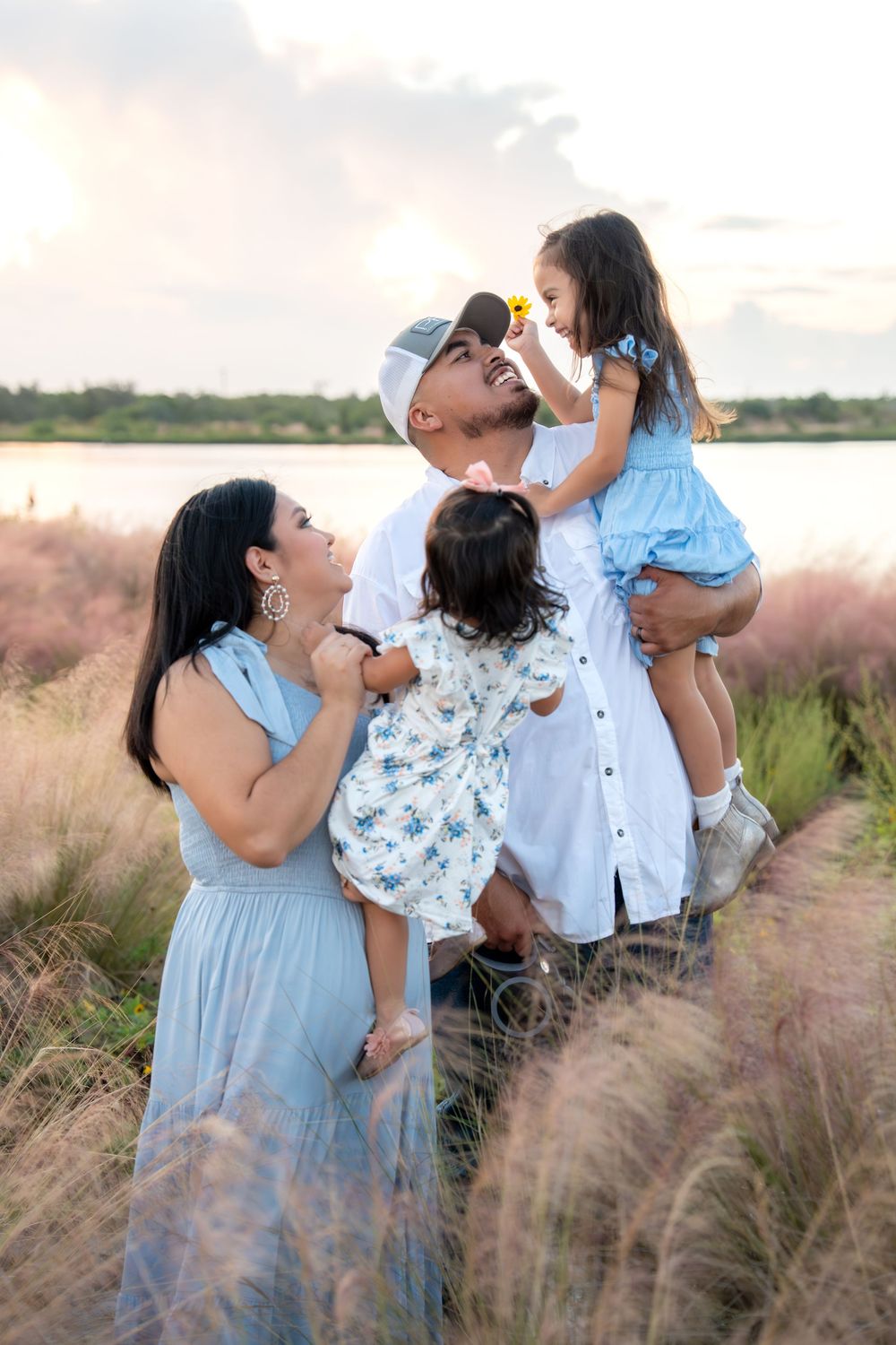Happy family with two young daughters in a field at sunset near a lake.