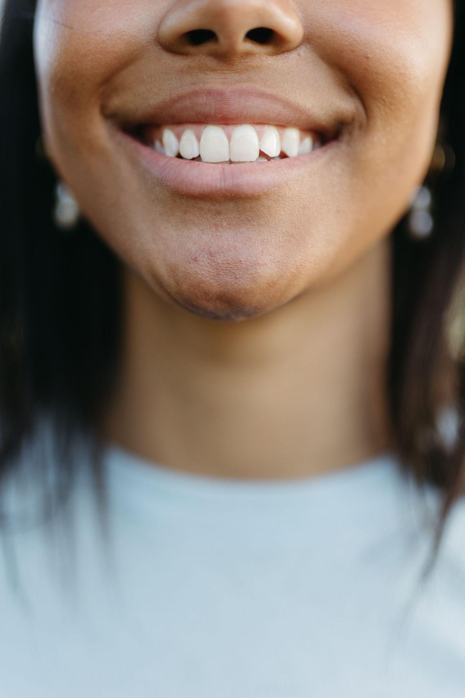 Close-up of a woman smiling with bright white teeth, wearing a light blue top and small earrings.