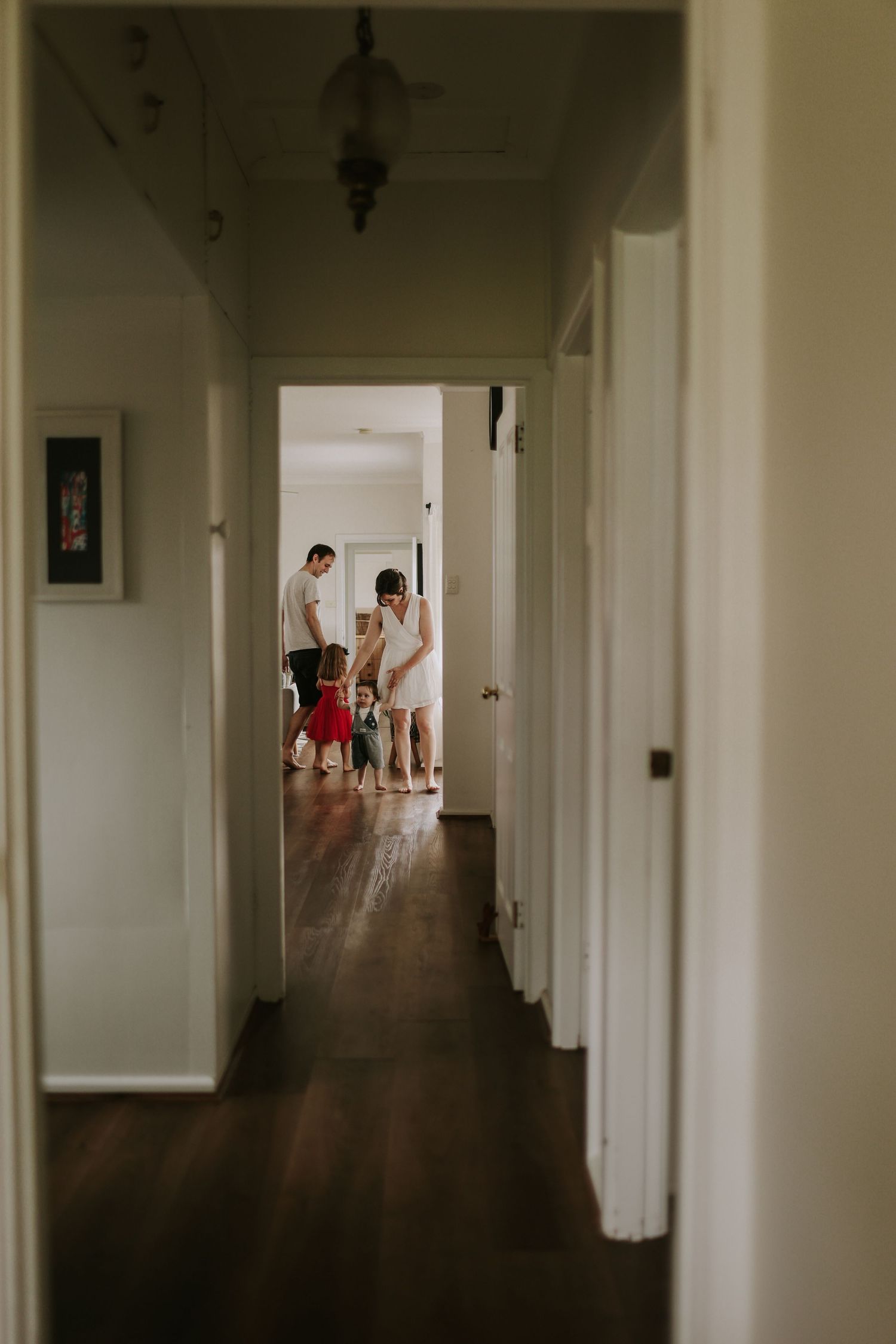 A family gathers in a sunlit room viewed through a narrow hallway with dark hardwood floors.