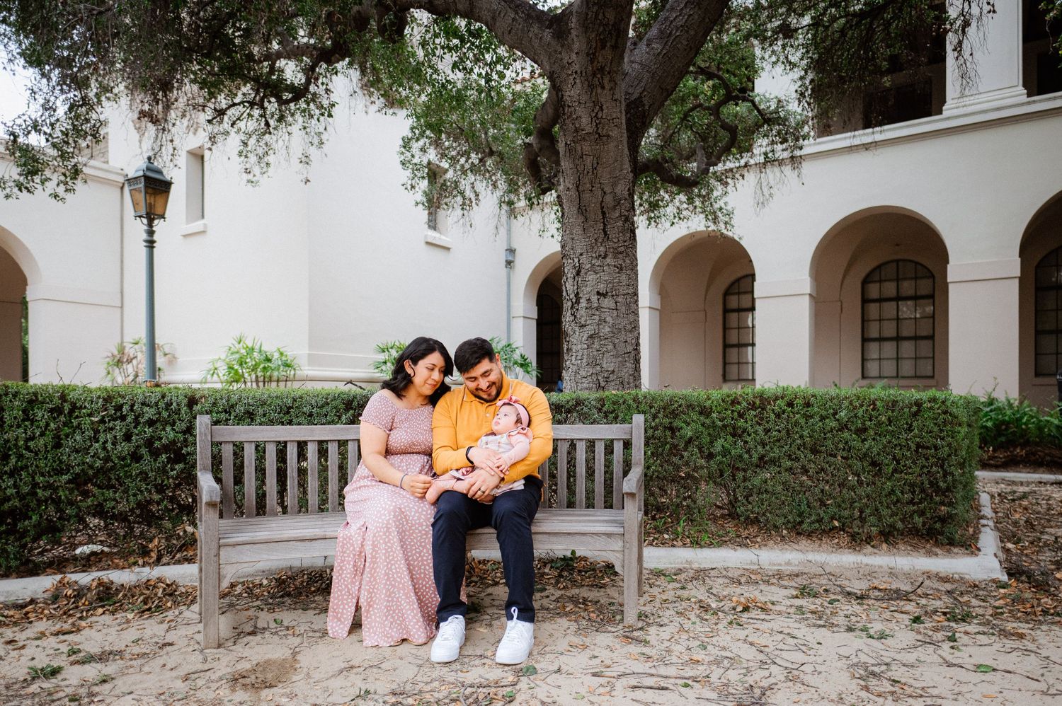 Family sitting together on bench in courtyard with Spanish colonial architecture.