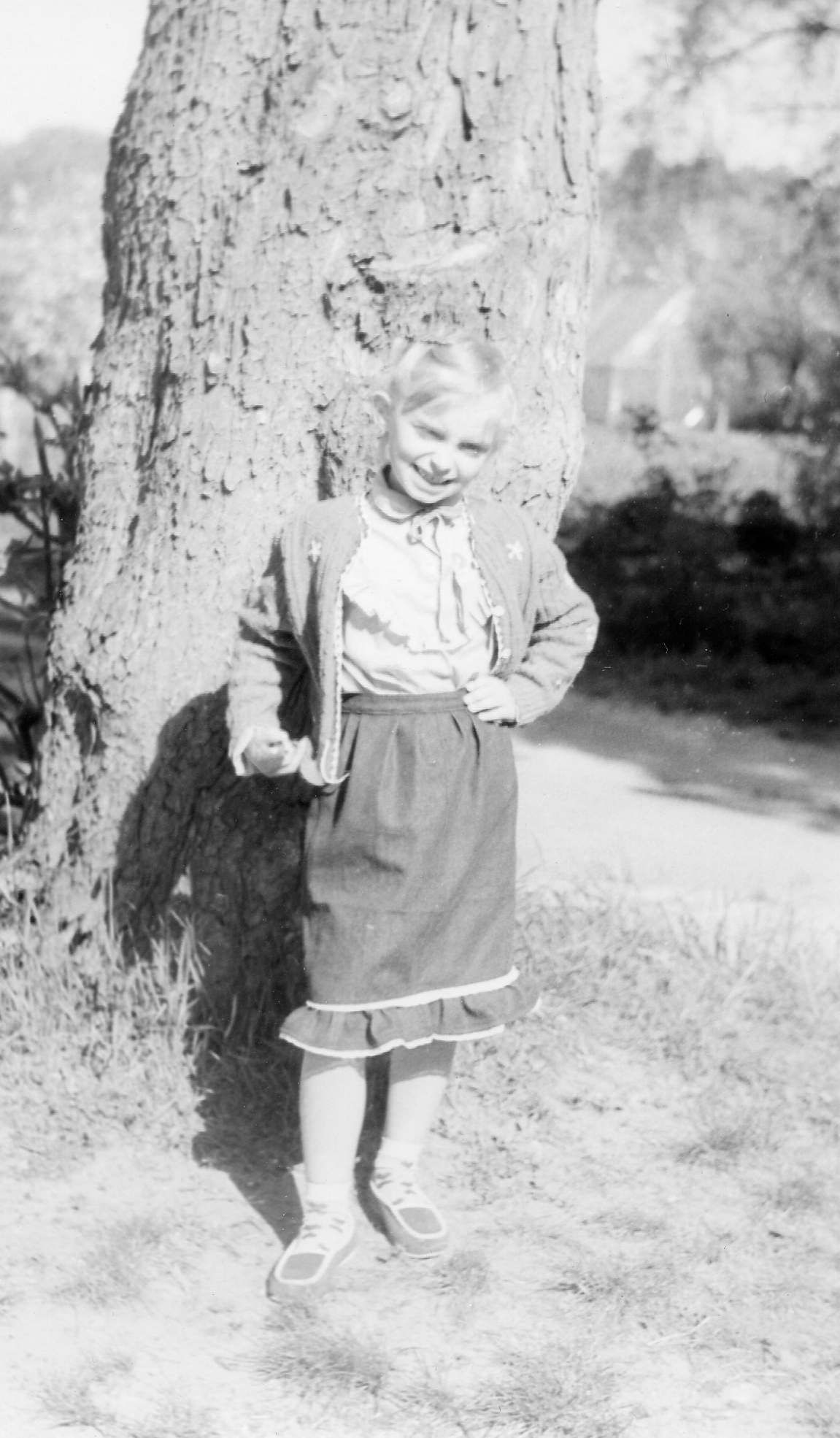 Black and white photograph as a Kasia Lussier as a little girl, standing in front of a tree.