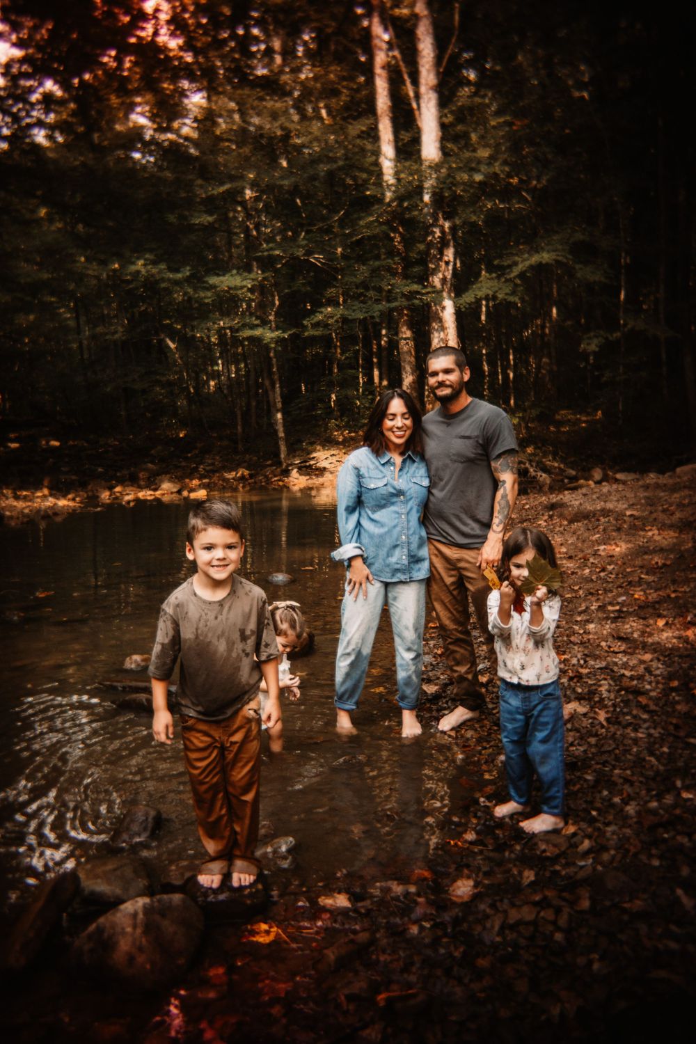 Family of four with a dog posing by a forest creek in autumn.