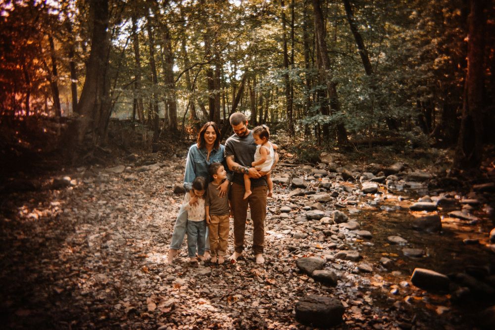 Family of four embraces in autumn forest by rocky stream.