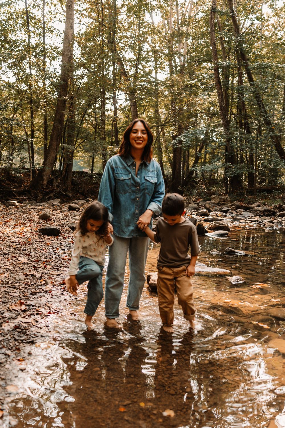 Smiling mother wading in rocky creek with two young children in forest.